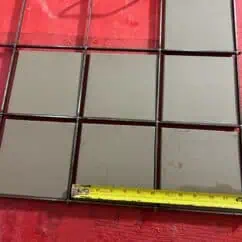 Metal grid frame with textured concrete tiles, measuring approximately 10 inches in width, placed on a red surface. Ideal for construction or tiling projects, showcasing durable material and precise dimensions.
