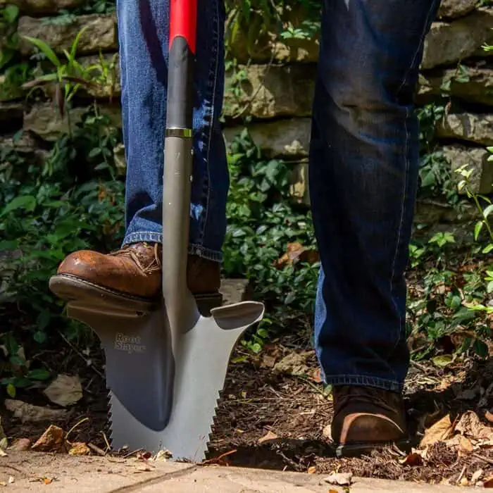 A person using a Root Slayer digging shovel outdoors, demonstrating gardening or landscaping tools, emphasizing durability and ergonomic design for professional or DIY garden projects.