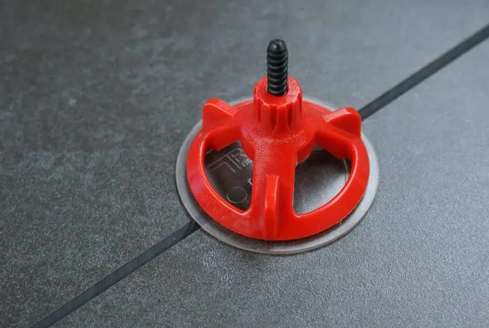 Red furniture leveling glide with a screw, used for adjusting and stabilizing home or office furniture on hard flooring.