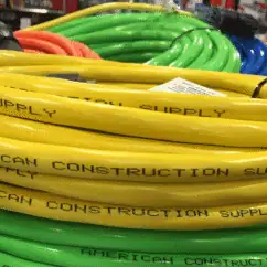 Yellow electrical supply hoses with "American Construction Supply" printed on them, coiled and stacked in a hardware store.
