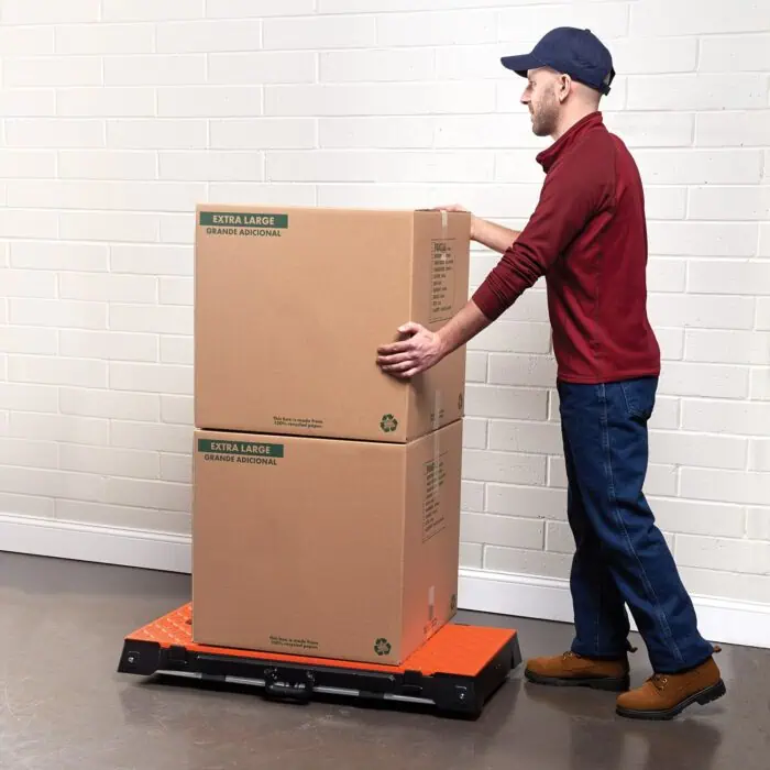 Stacks of large cardboard boxes labeled "EXTRA LARGE" ready for shipping or storage, placed on a digital pallet scale against a white brick wall, emphasizing packing and logistics.