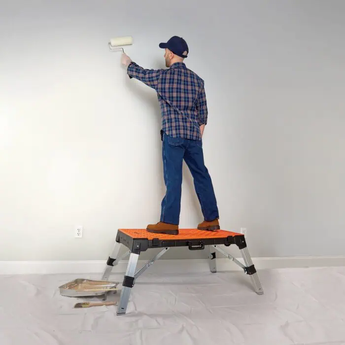 Man painting wall with roller on step stool, home improvement, interior painting, DIY renovation, painting tools, maintaining walls, residential painting, professional painter, wall decor.