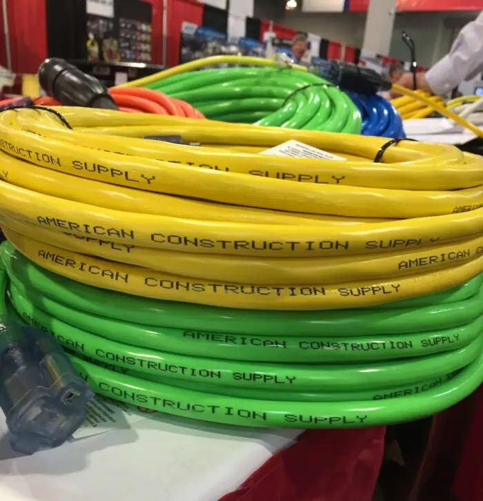Yellow, green, and blue electrical cables with "American Construction Supply" printed on them, coiled on display at a hardware store.
