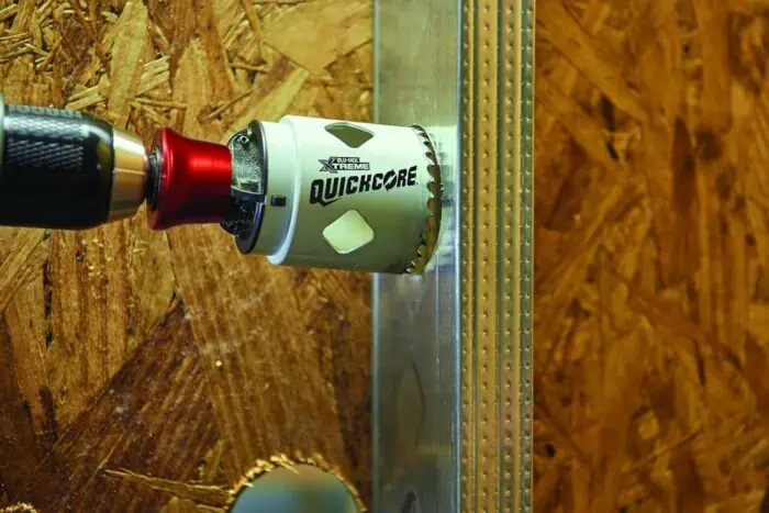 High-precision hole saw attached to a power drill on a wooden surface, featuring the "Quickcore" logo for wood cutting tools.