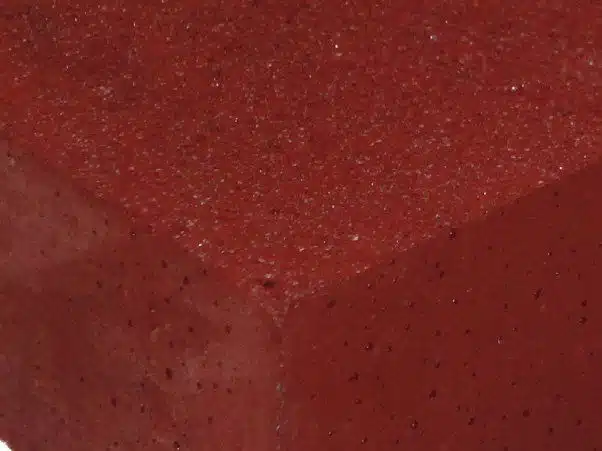 Red foam close-up with textured surface and small black specks, suitable for sports or cushioning applications.