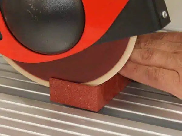 Nylon abrasive wheel cutting red sanding block on metal work surface.